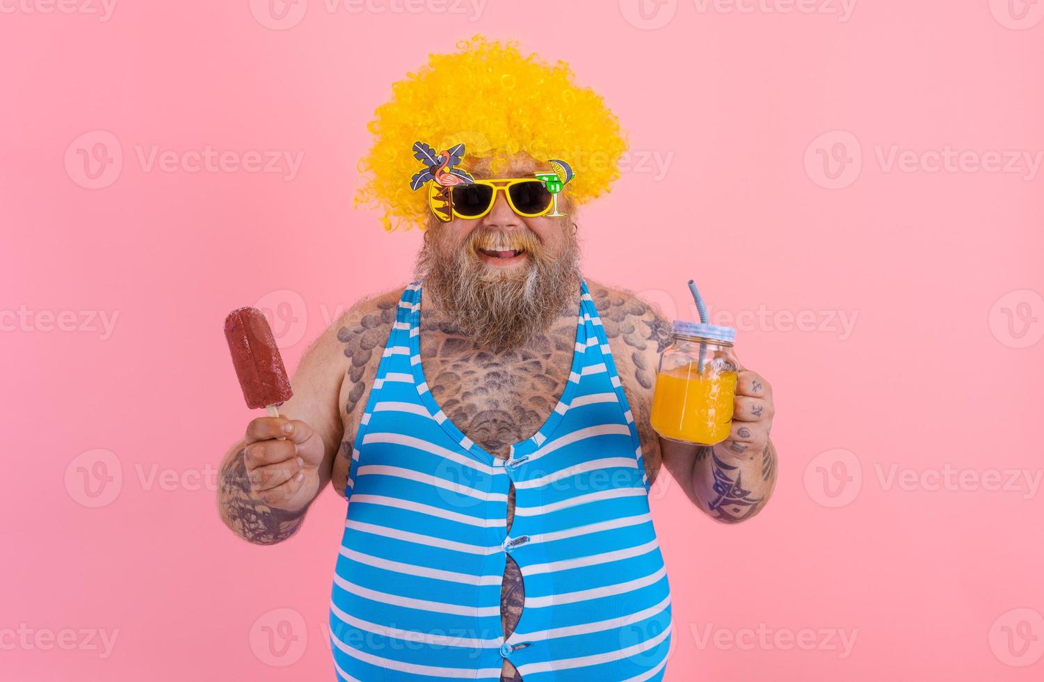 Fat happy man with beard and wig eats a popsicle and drinks a juice fruit photo