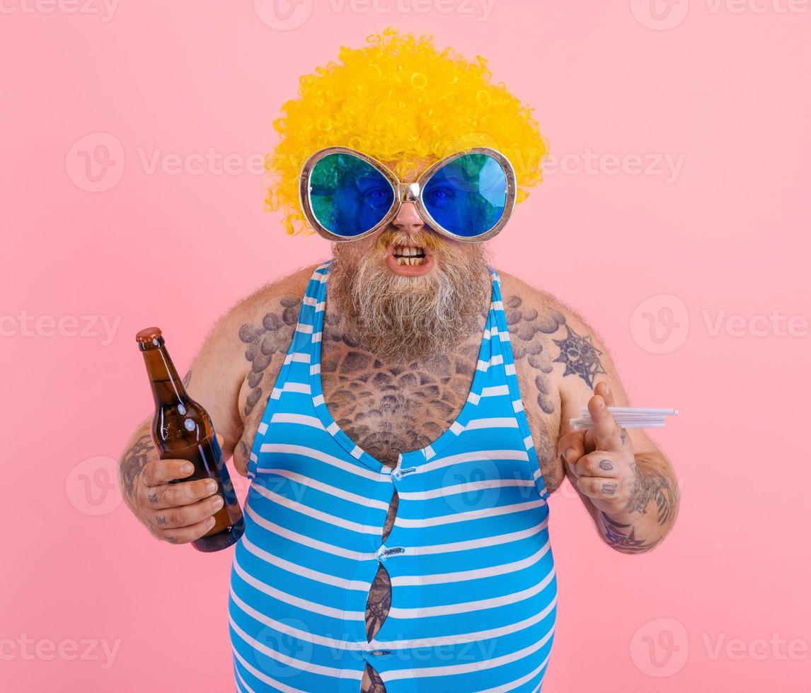 Fat man with beard and wig smokes cigarettes and drinks beer photo