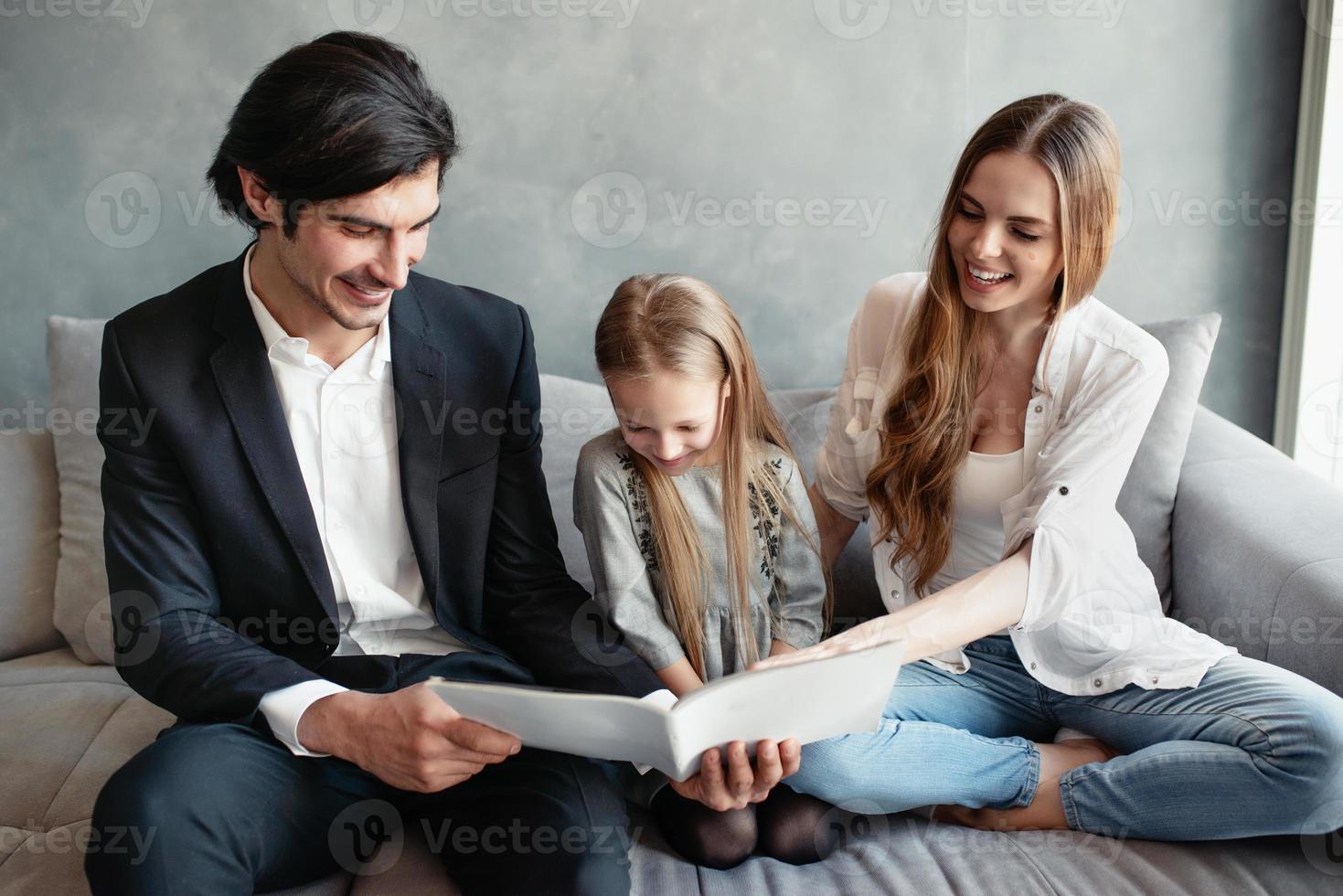 contento pequeño niña lee un libro con su padres foto