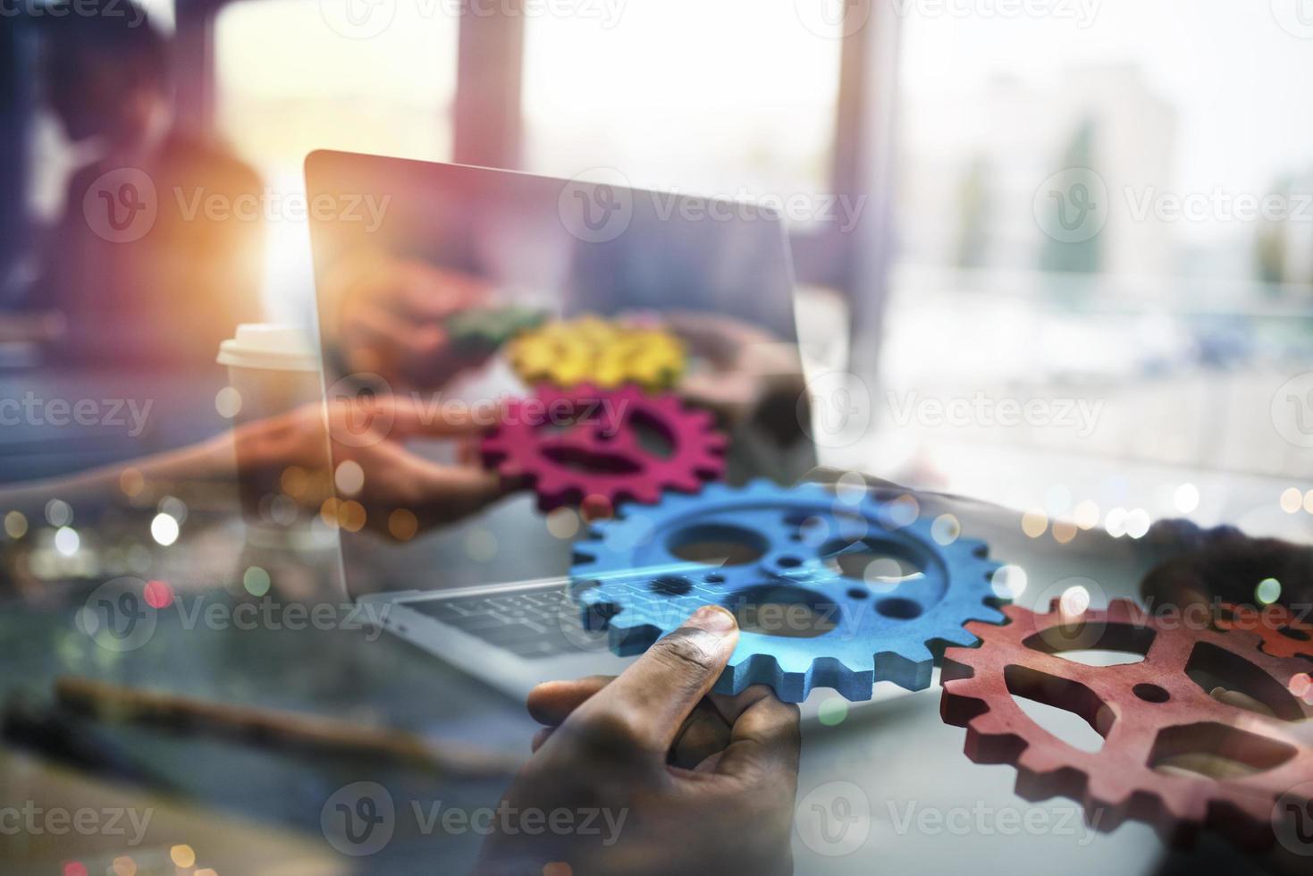 negocio personas con engranajes en mano ese salida desde un ordenador portátil. concepto de remoto cooperación y trabajo en equipo. doble exposición foto