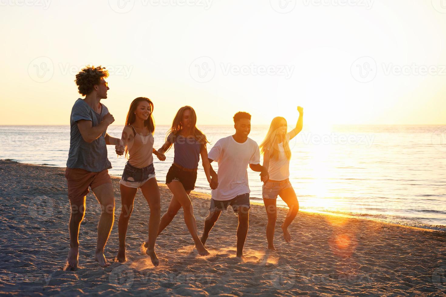 Group of happy friends having fun at ocean beach at dawn photo