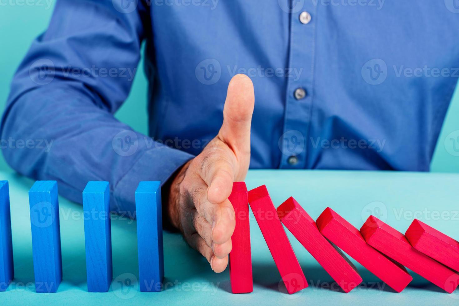 Businessman stops a chain fall like domino game. Concept of preventing crisis and failure in business. photo