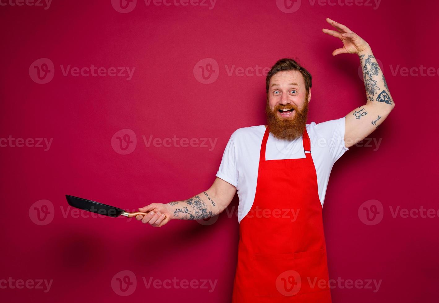 Happy chef with beard and red apron cooks with pan photo