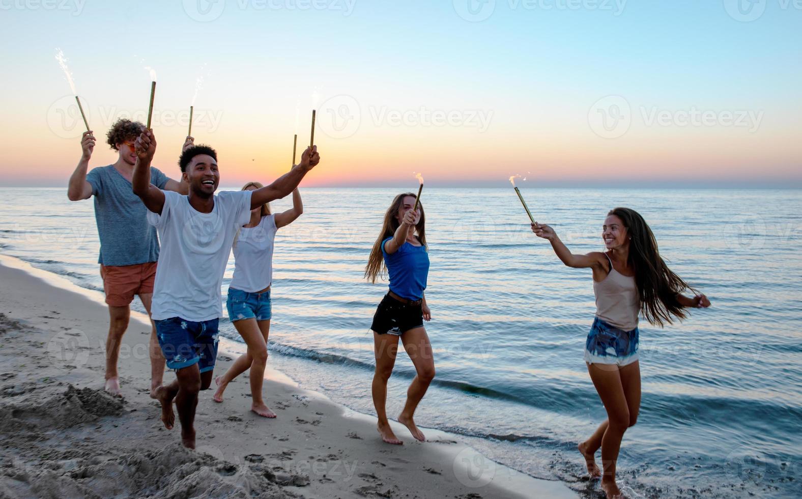 Happy smiling friends running at the beach with sparkling candles photo