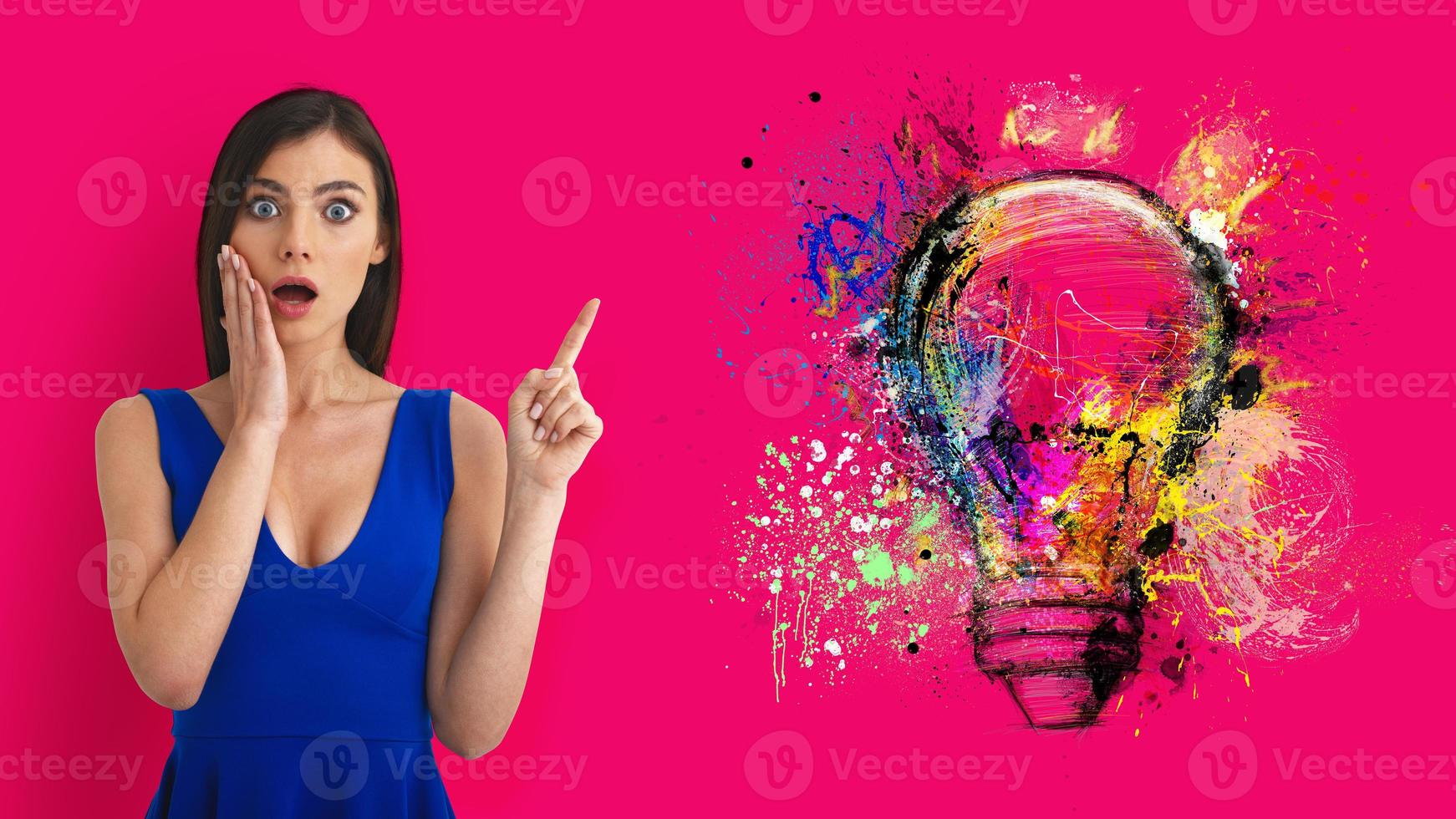 Surprised woman pointing at big stylized light bulb on magenta background. Concept of idea and creativity photo