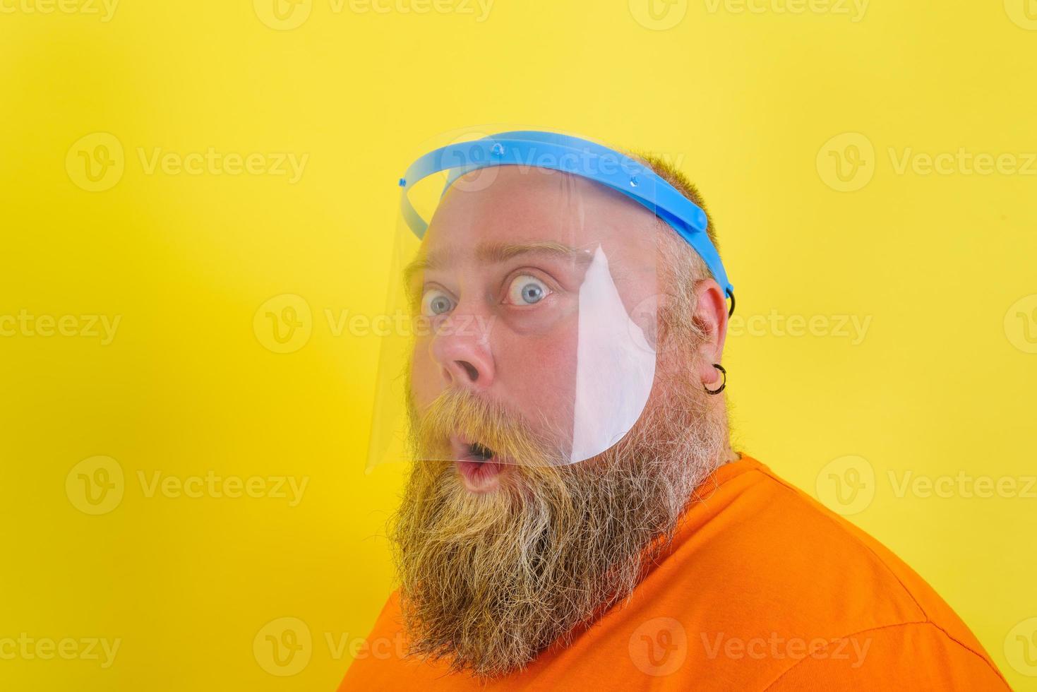 Amazed man with beard and tattoos wears a protective face shield against covid-19 photo