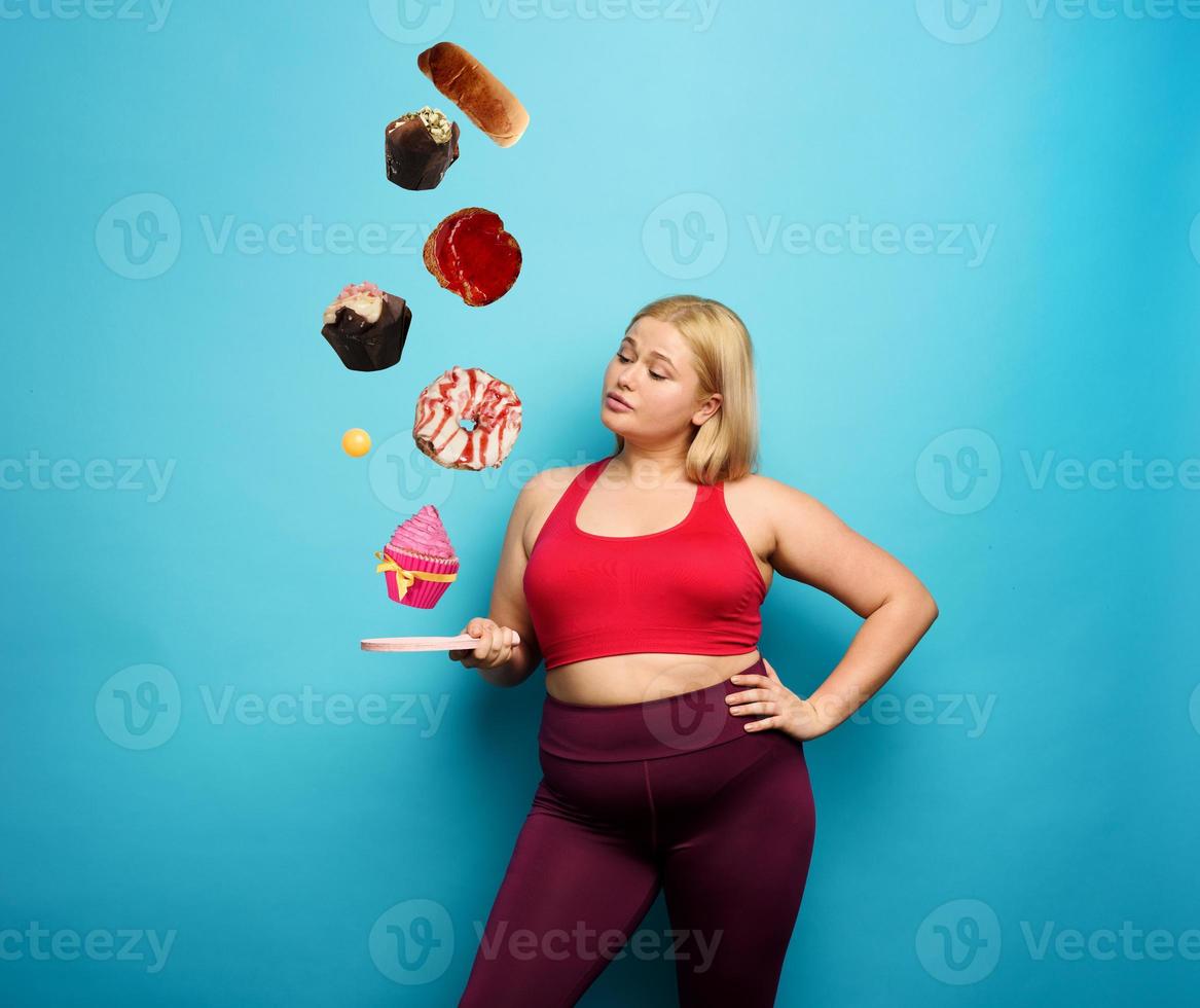 Fat girl tries to play with table tennis but thinks always to eat. Cyan background photo