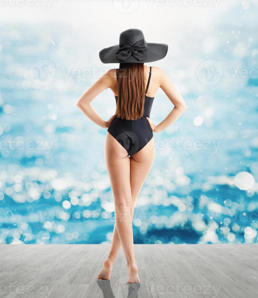 Woman in elegant black hat and swimsuit looks at sea photo