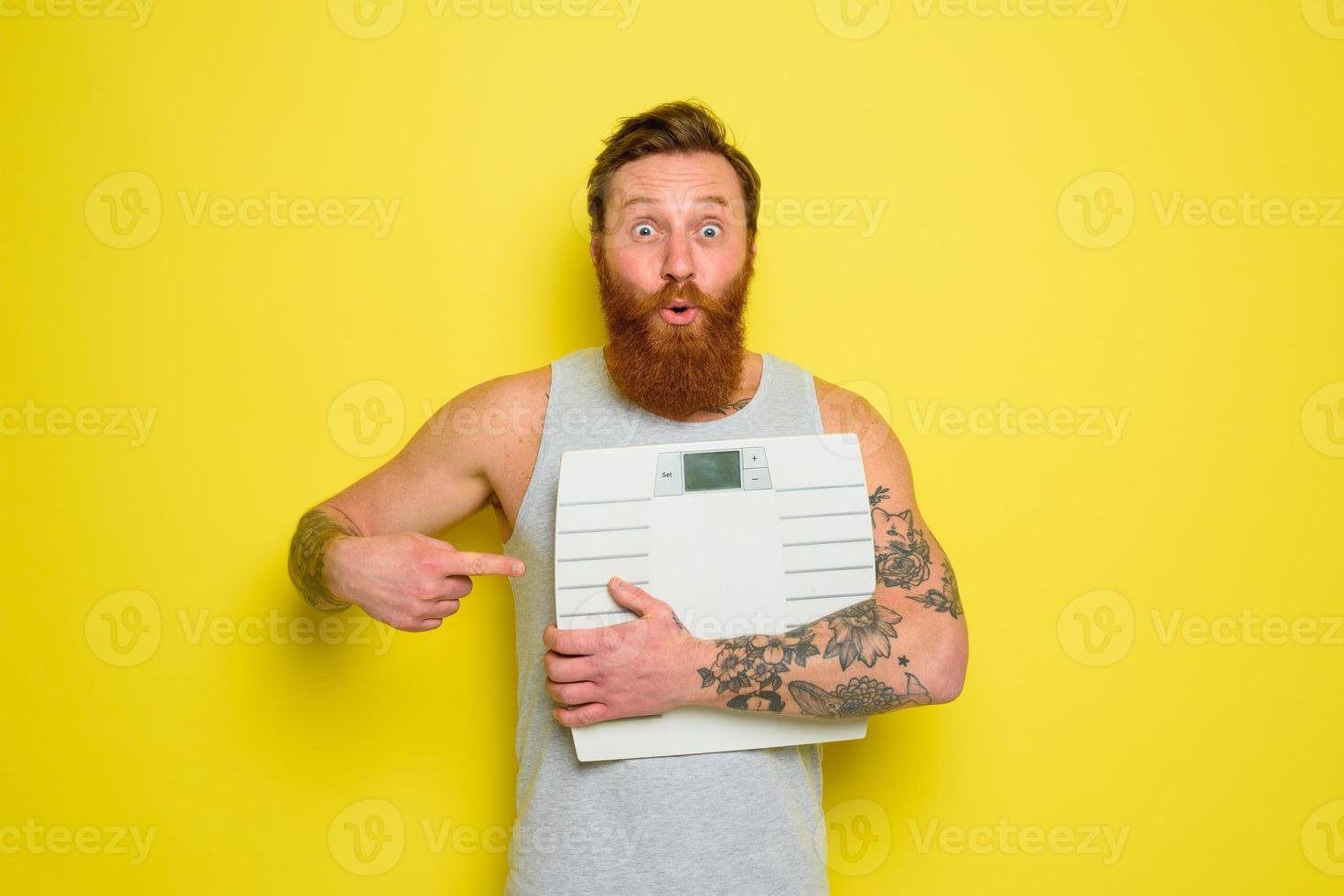 Amazed man with beard and tattoos holds an electronic balance photo