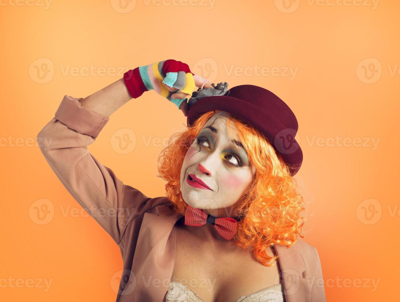 Pensive clown girl with too many questions. Orange background photo