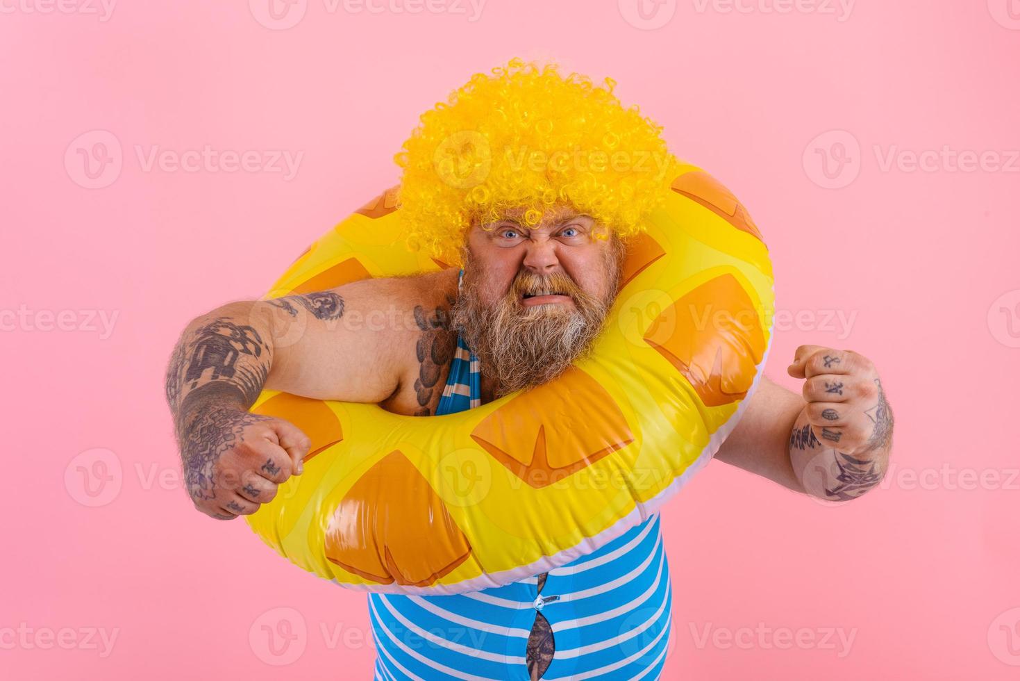 Fat angry man with wig in head is ready to swim with a donut lifesaver photo