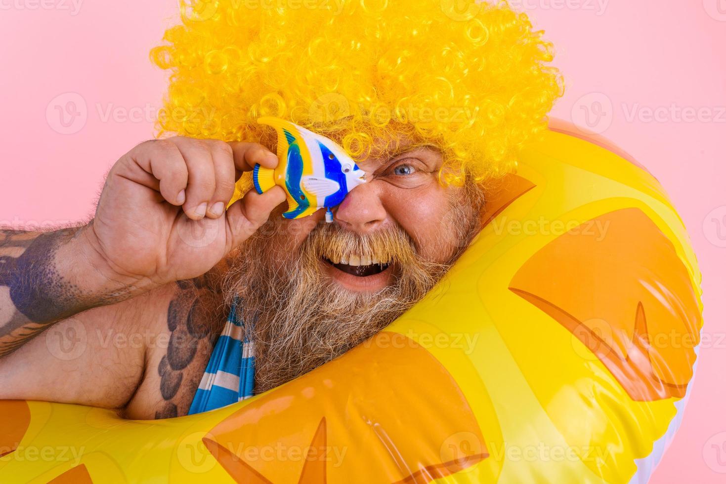 Fat happy man with wig in head is ready to swim with a donut lifesaver photo