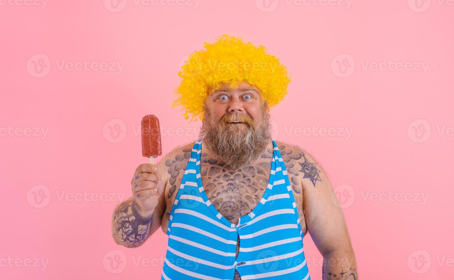 Fat amazed man with beard and wig eats a popsicle photo