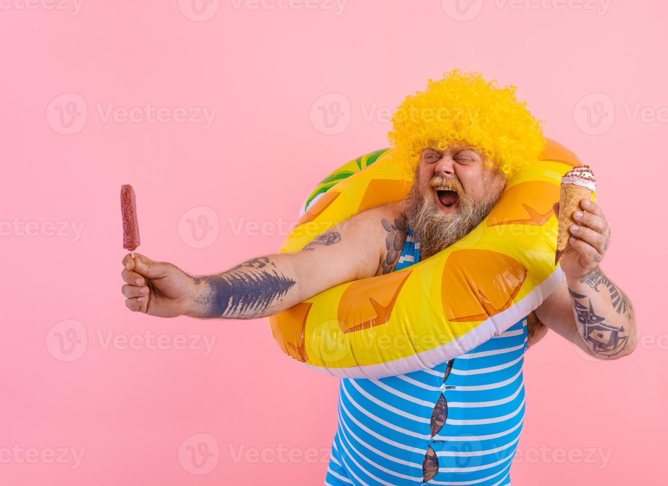 Fat man with beard and wig eats a popsicle and an icecream photo