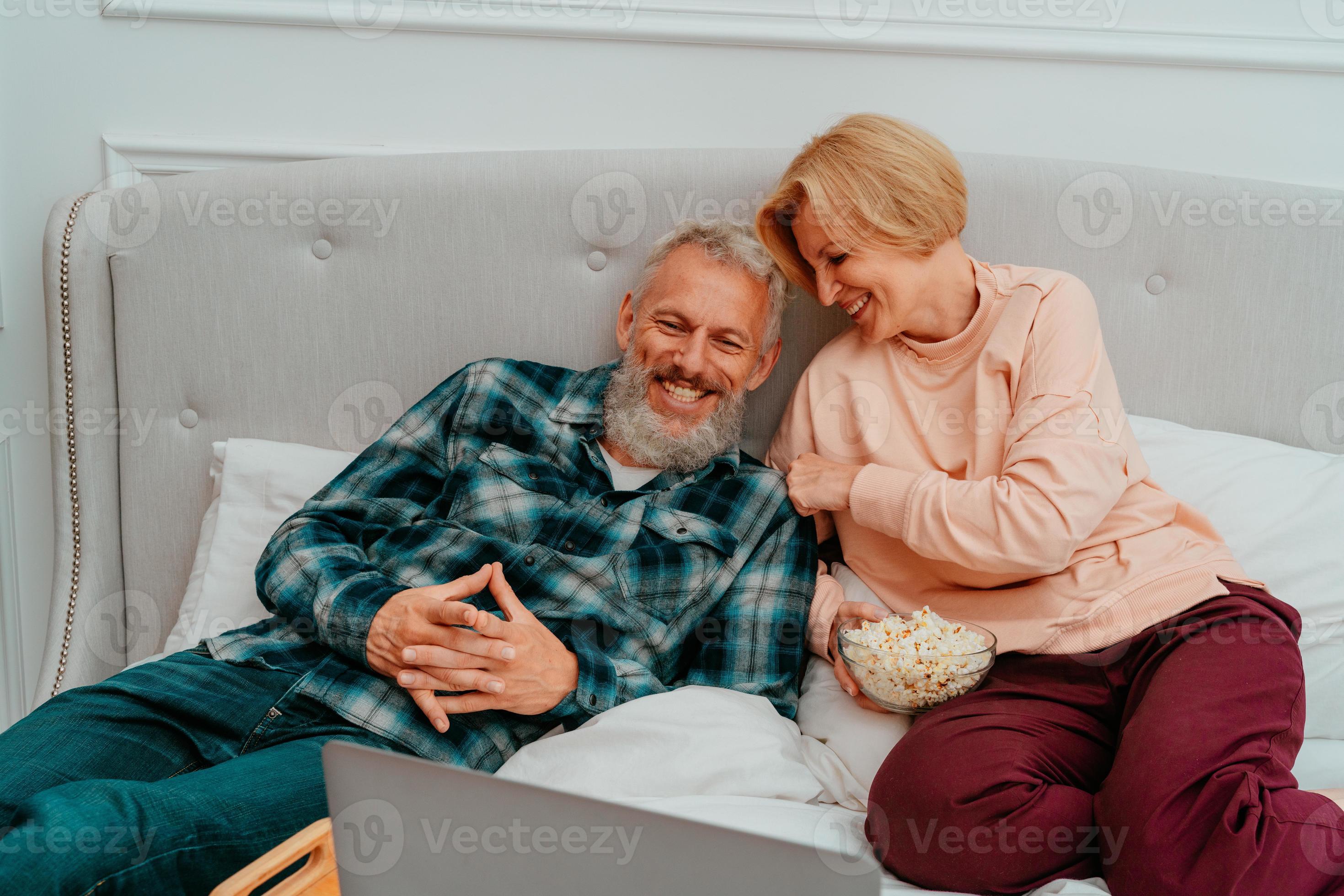 Husband and wife watch a film on the bed and eat popcorn 20726597 Stock Photo at Vecteezy