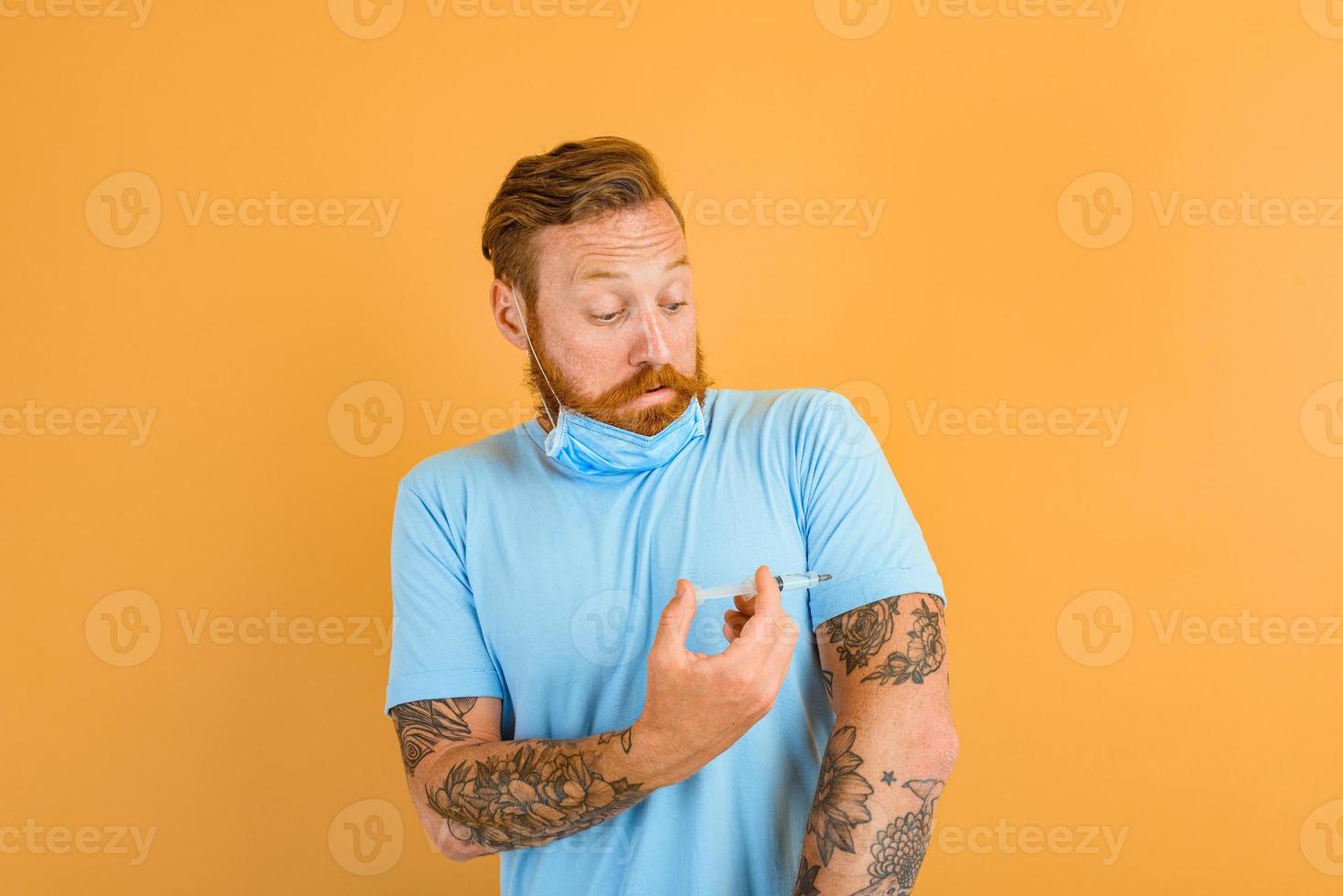 Afraid man with beard, tattoo and mask for covid-19 is ready for the virus vaccine photo