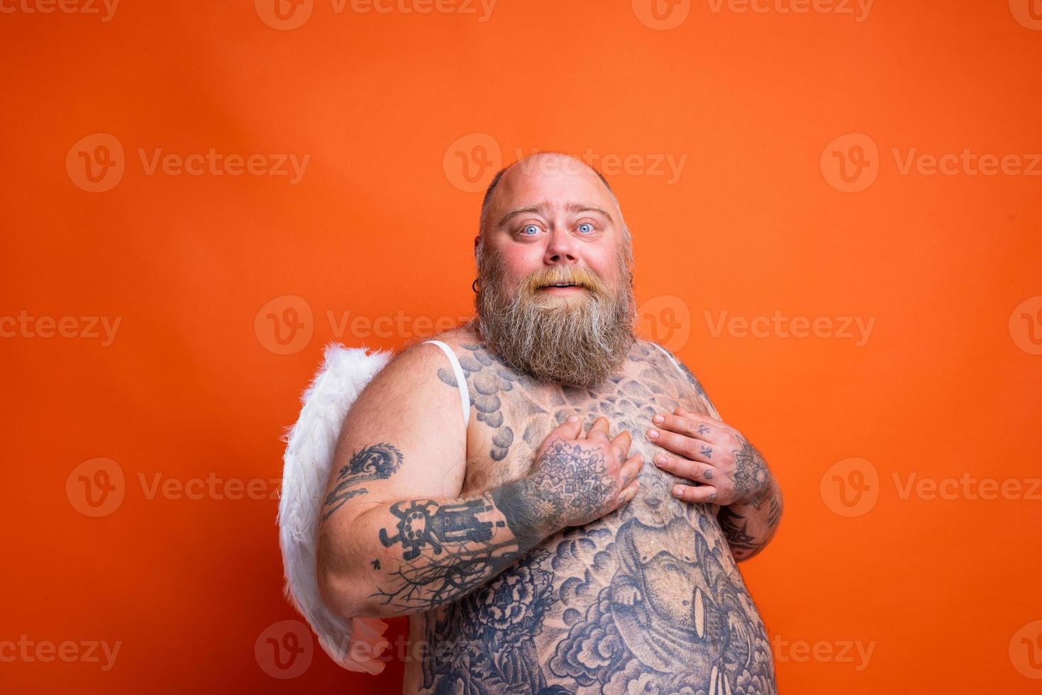 Fat amazed man with beard ,tattoos and wings acts like an angel photo