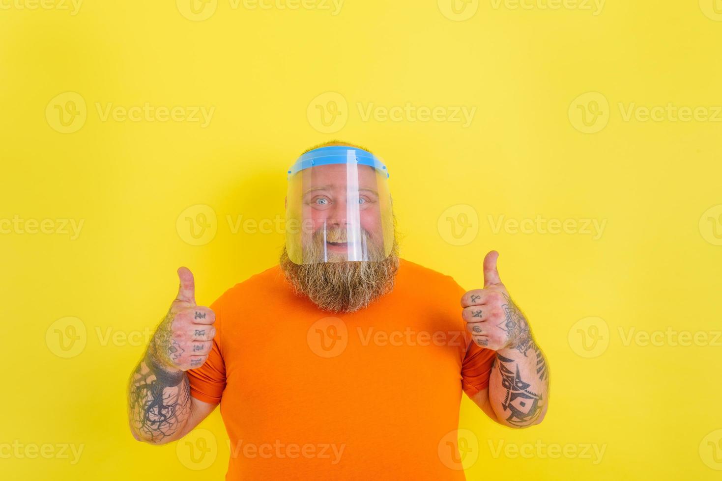 Happy man with beard and tattoos wears a protective face shield against covid-19 photo