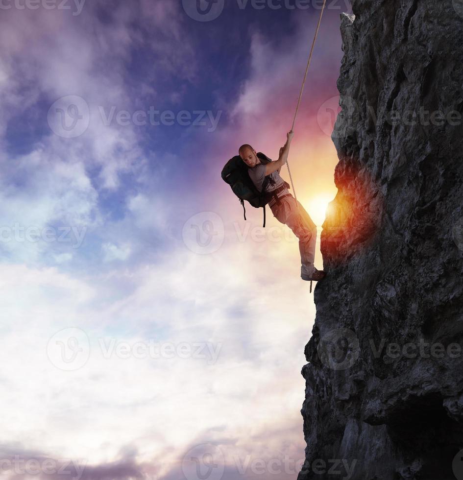 Man climbs a high danger mountain with a rope during sunset photo