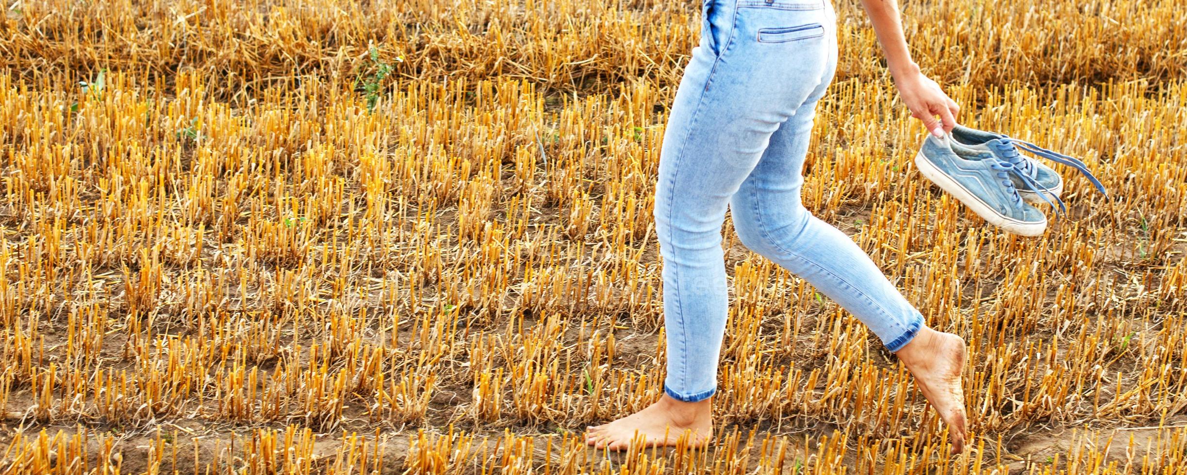 barefoot girl with sneakers in hand walking in the agricultural field with haystack and bales photo