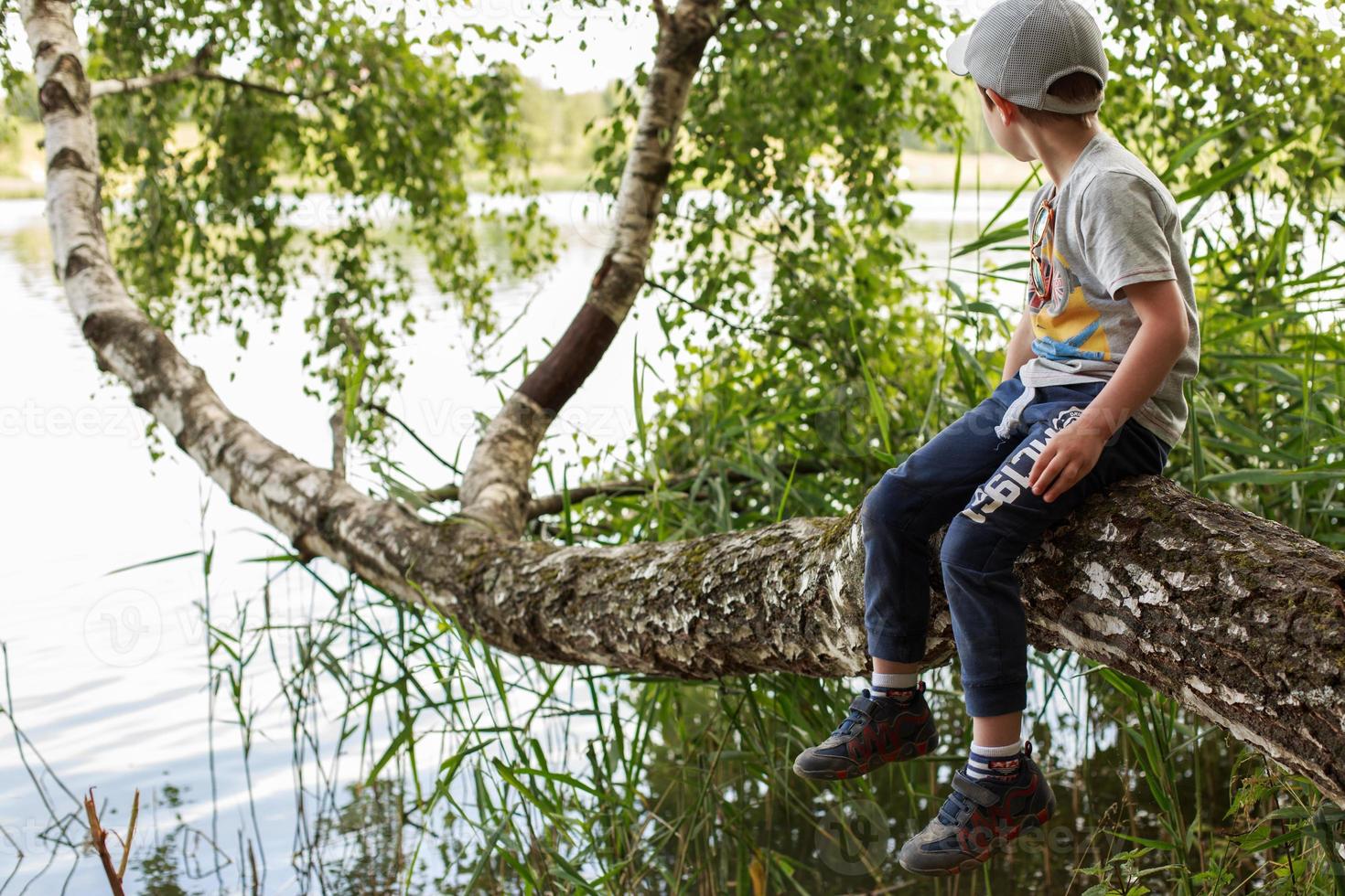 the boy sits on a tree by the lake photo