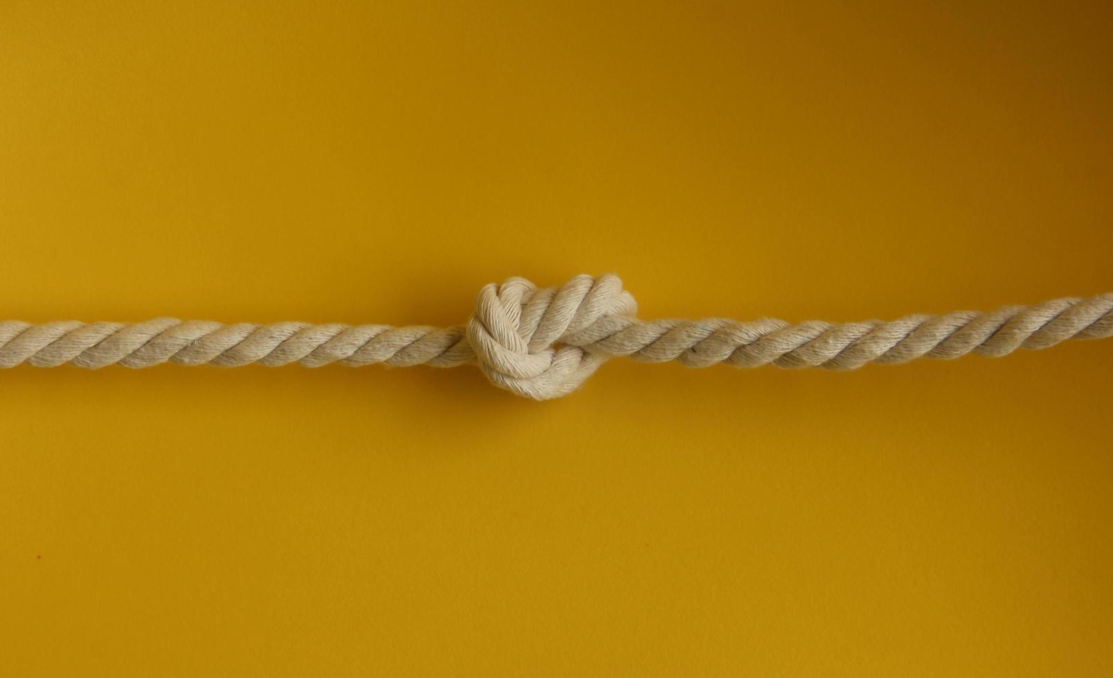 Strong white thick braided sailing or art crafting rope photo isolated on plain yellow background. Tied up rope knot.