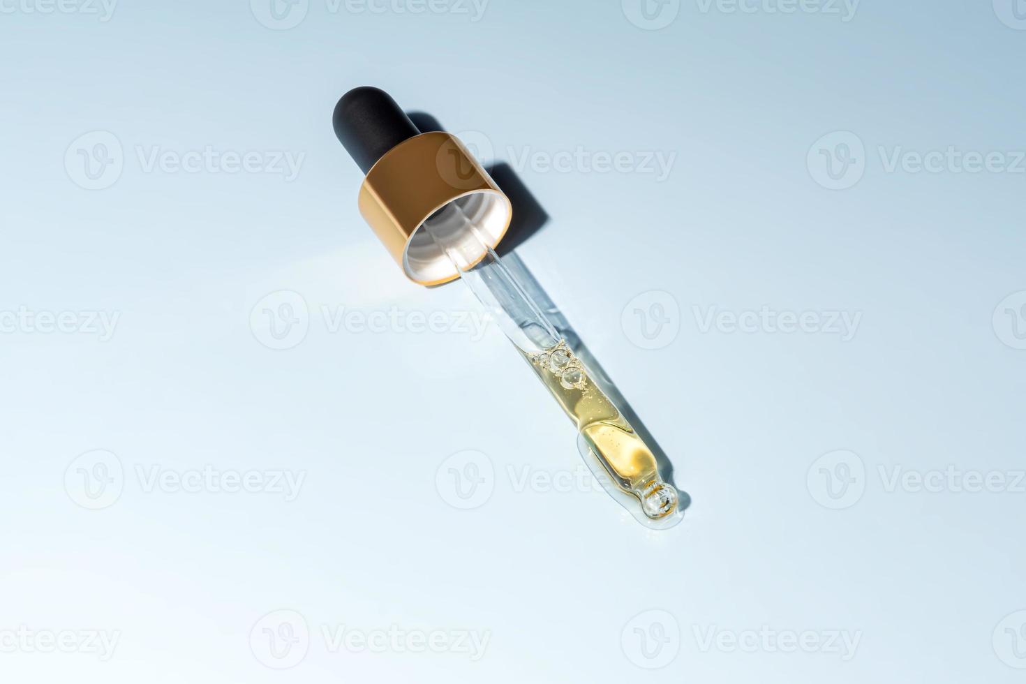 beauty face oil dripping from gold dropper on blue background. Skin care cosmetic advertisement with copy space photo