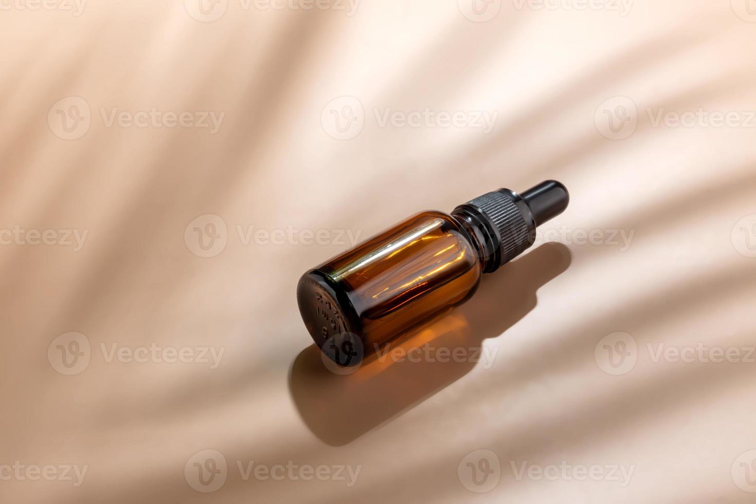 Dark glass cosmetic bottle with a dropper on a beige background with tropical leaves shadow. Natural cosmetics concept, natural essential oil and skin care products photo