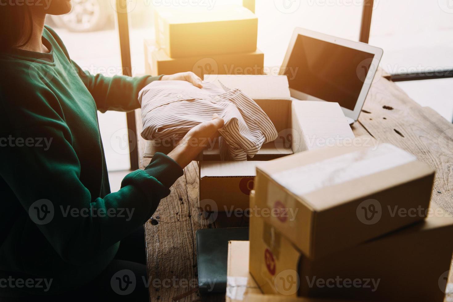 Startup SME small business entrepreneur of freelance Asian woman wearing apron using laptop and box to receive and review orders online to prepare to pack sell to customers, online sme business ideas. photo