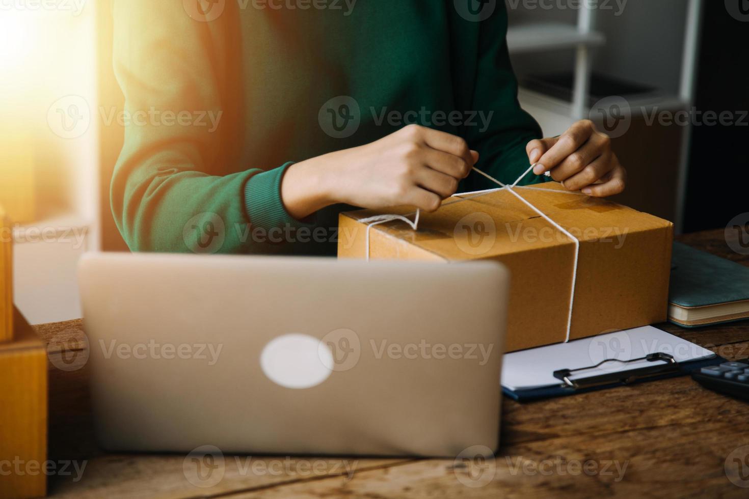 Startup SME small business entrepreneur of freelance Asian woman wearing apron using laptop and box to receive and review orders online to prepare to pack sell to customers, online sme business ideas. photo