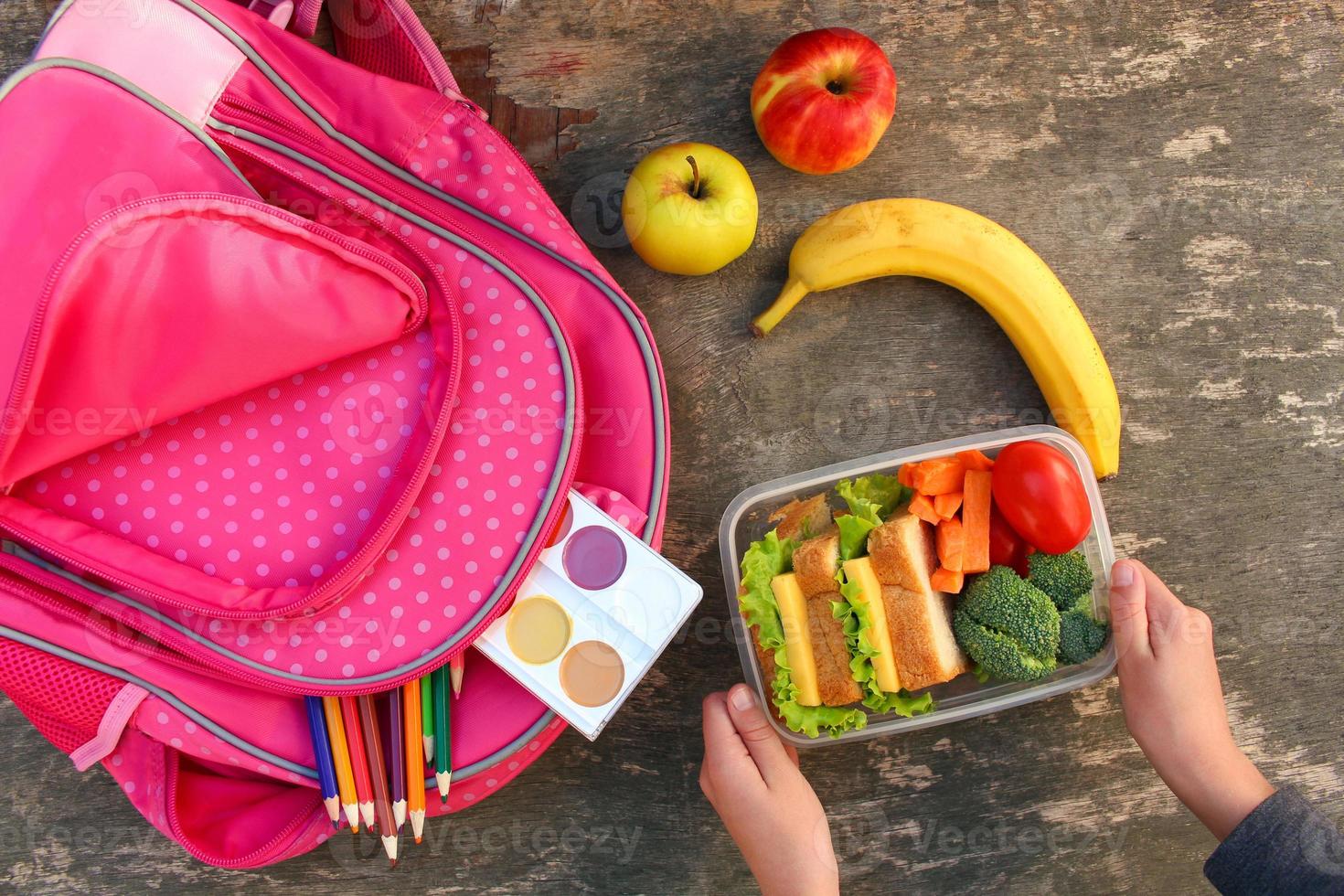 Sandwiches, fruits and vegetables in food box, backpack on old wooden background. Concept of child eating at school. Top view. Flat lay. photo