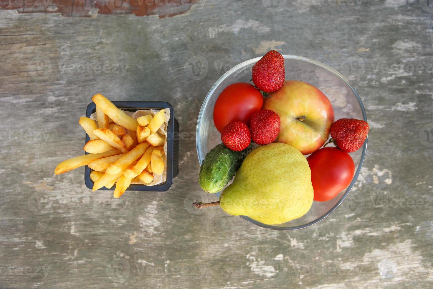 French fries, fruits, vegetables on old wooden background. Concept choosing correct nutrition or of junk eating. Top view. photo