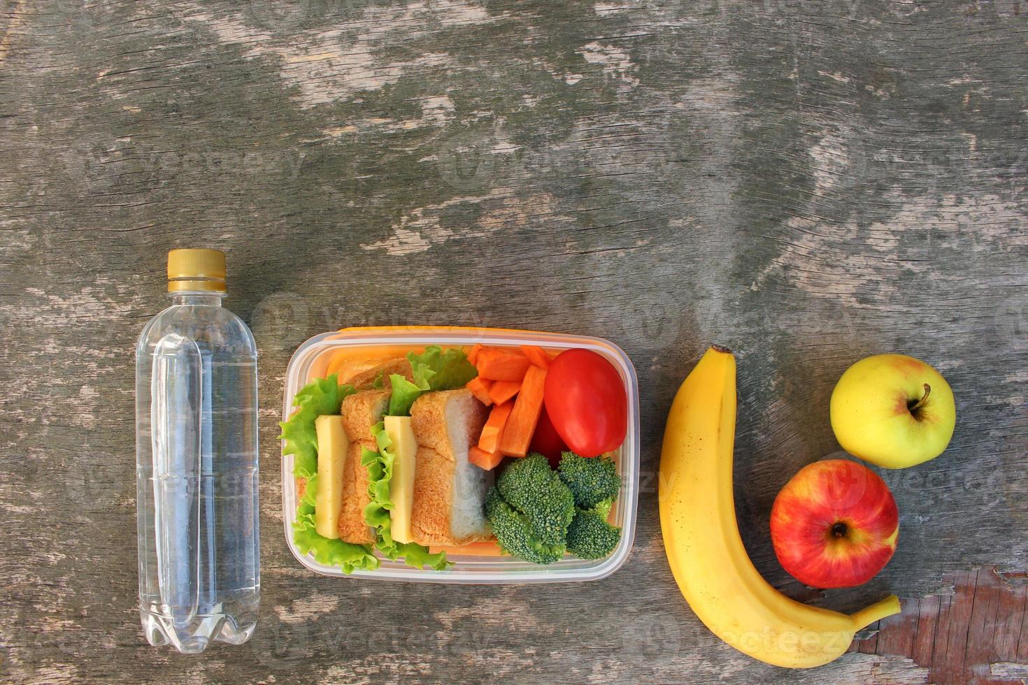 sándwiches, frutas y verduras en caja de comida, agua sobre fondo de madera vieja. vista superior. endecha plana foto