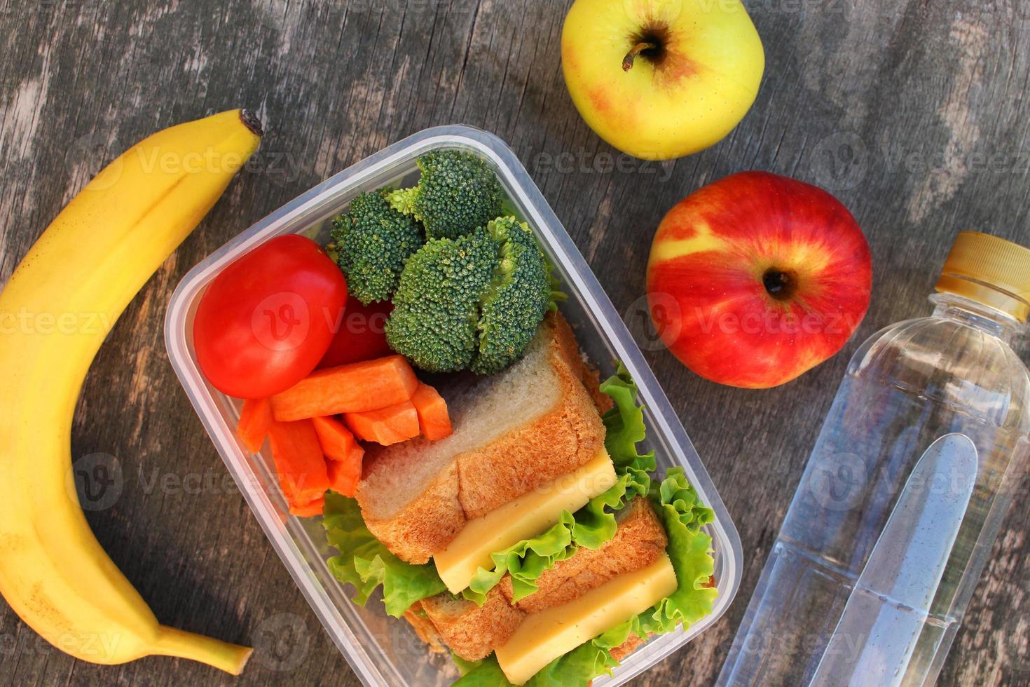 Sandwiches, fruits and vegetables in food box, water on old wooden background. Top view. Flat lay. photo