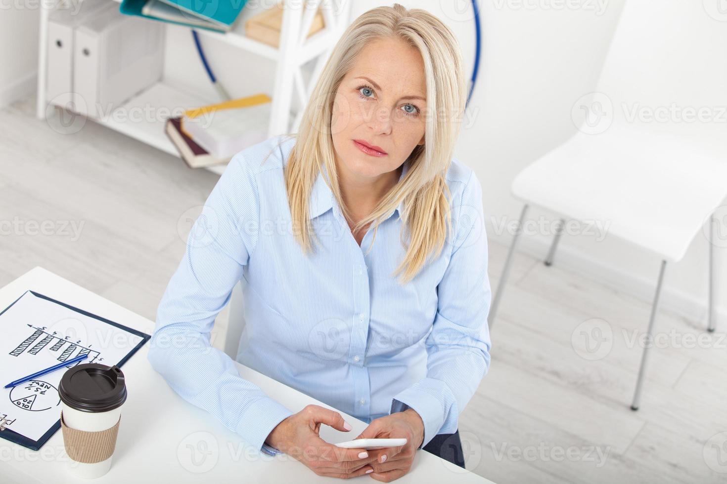 Working on new project. Business woman working in office with documents. Beautiful middle aged woman looking at laptop with smile while siting in the office. photo