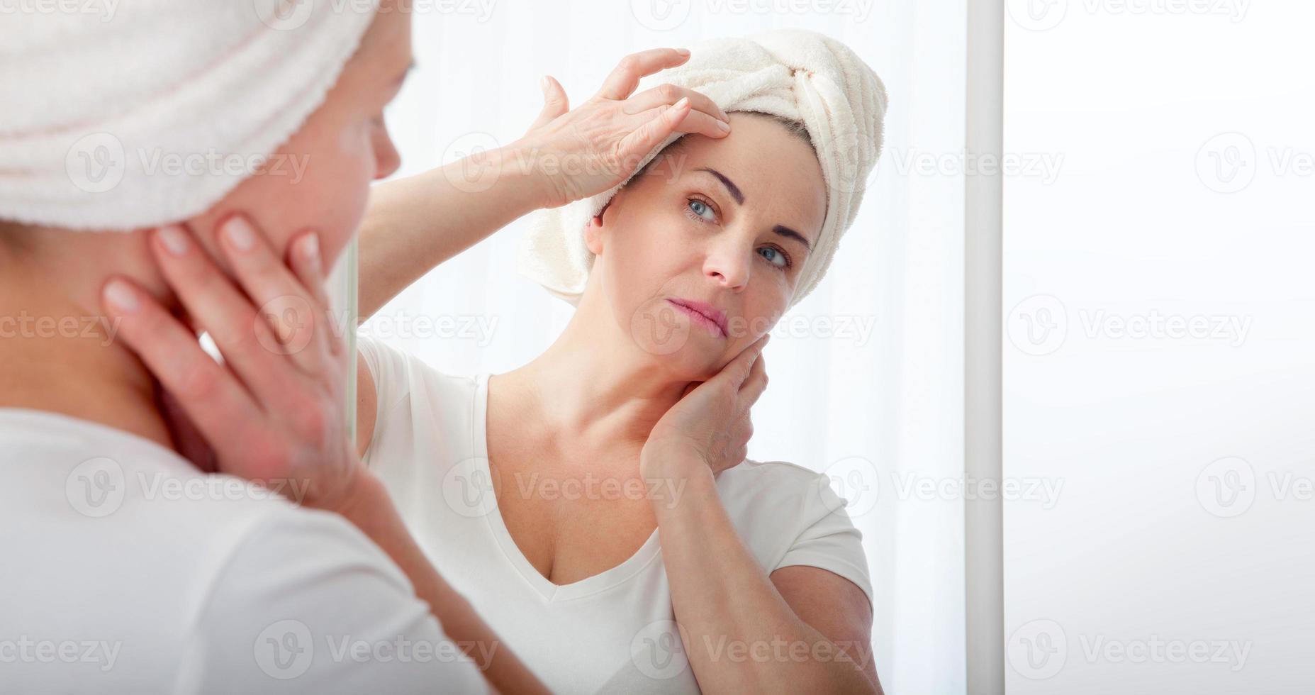 Forty years old woman looking at wrinkles in mirror. Plastic surgery and collagen injections. Makeup. Macro face. Selective focus on the face. photo