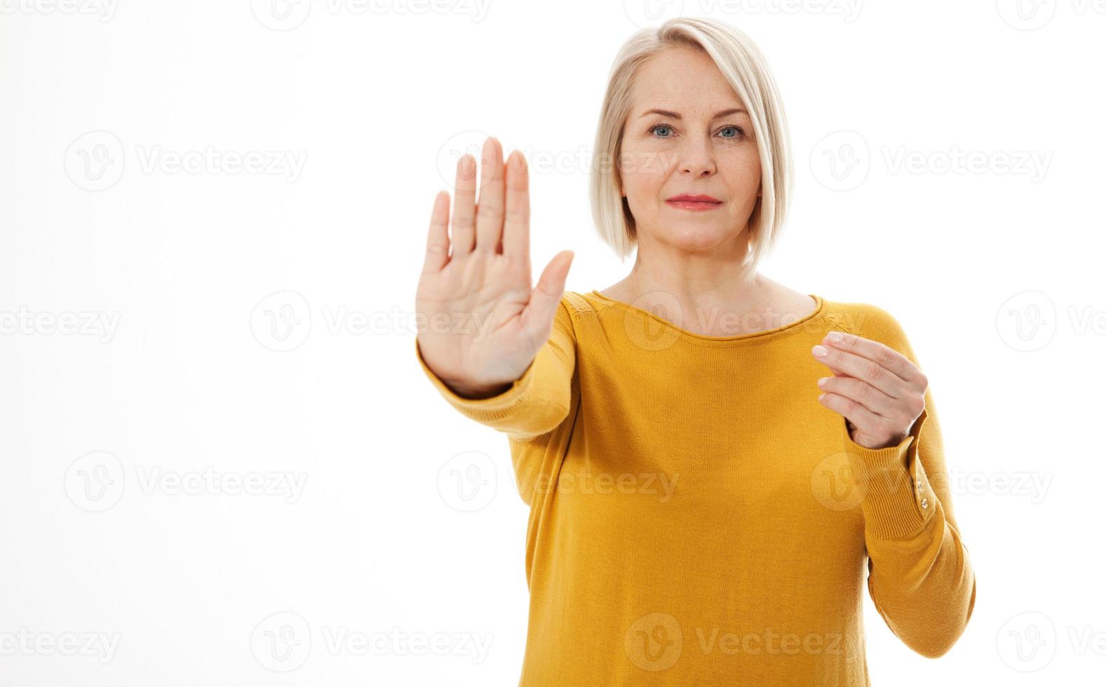 Attractive middle aged woman in a bright yellow sweater holds an empty hand for an anti-advertisement product. Excited woman showing the sign of stop photo