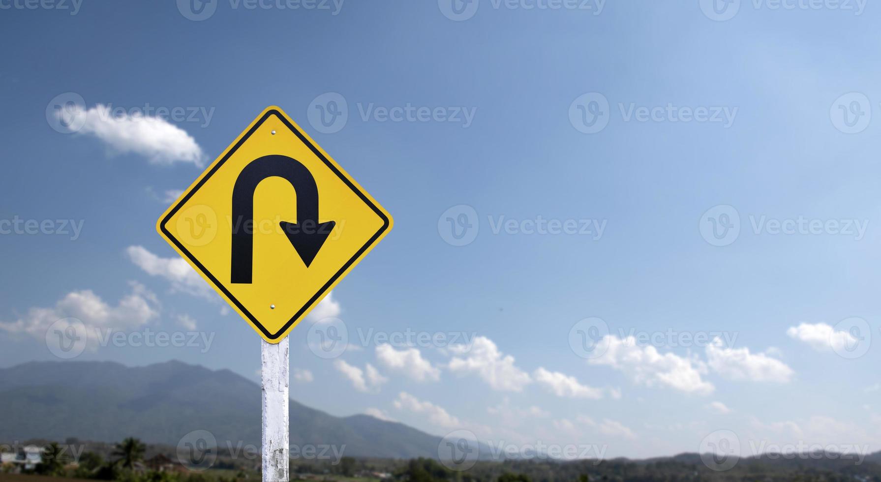 Traffic sign, right U turn sign on cement pole beside the rural road with white cloudy bluesky background, copy space. photo