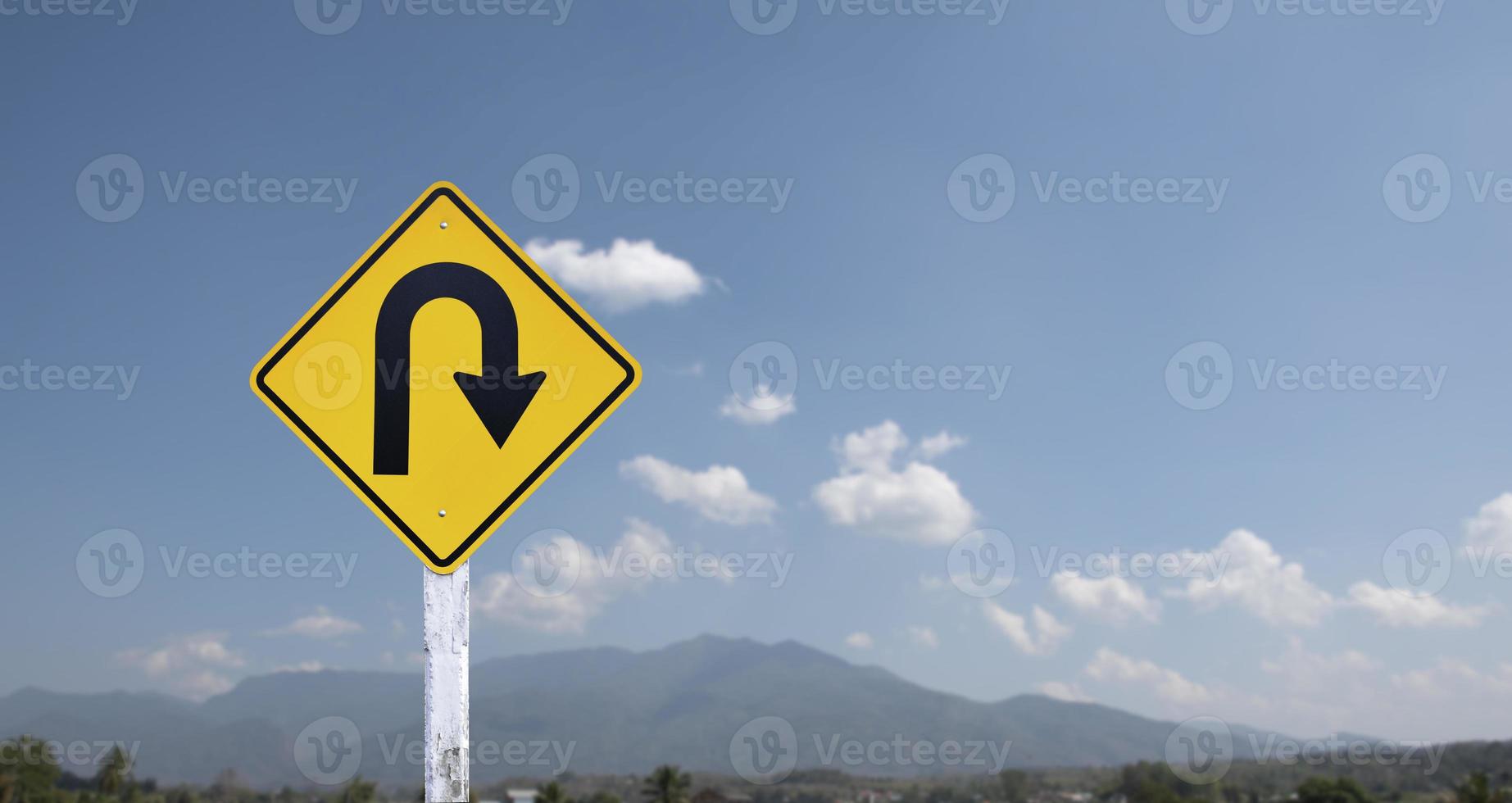 Traffic sign, right U turn sign on cement pole beside the rural road with white cloudy bluesky background, copy space. photo