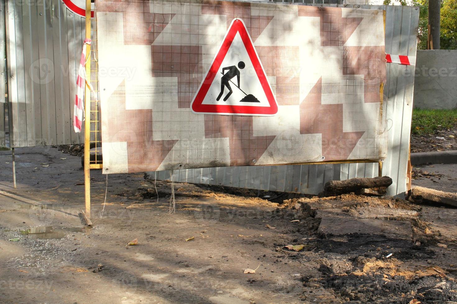 Construction road triangle sign on metal fence background. Preparation for laying new asphalt pavement. Rework and repair  concept. Traffic tape striped warning lines on a street. Prohibition board photo