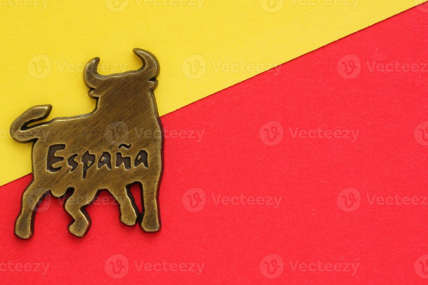 Metal souvenir fridge magnet of bull with word Spain on spanish on red and yellow background. Travel memory concept. Gift typical product for tourists from trip. Top view, flatlay. Copy space for text photo