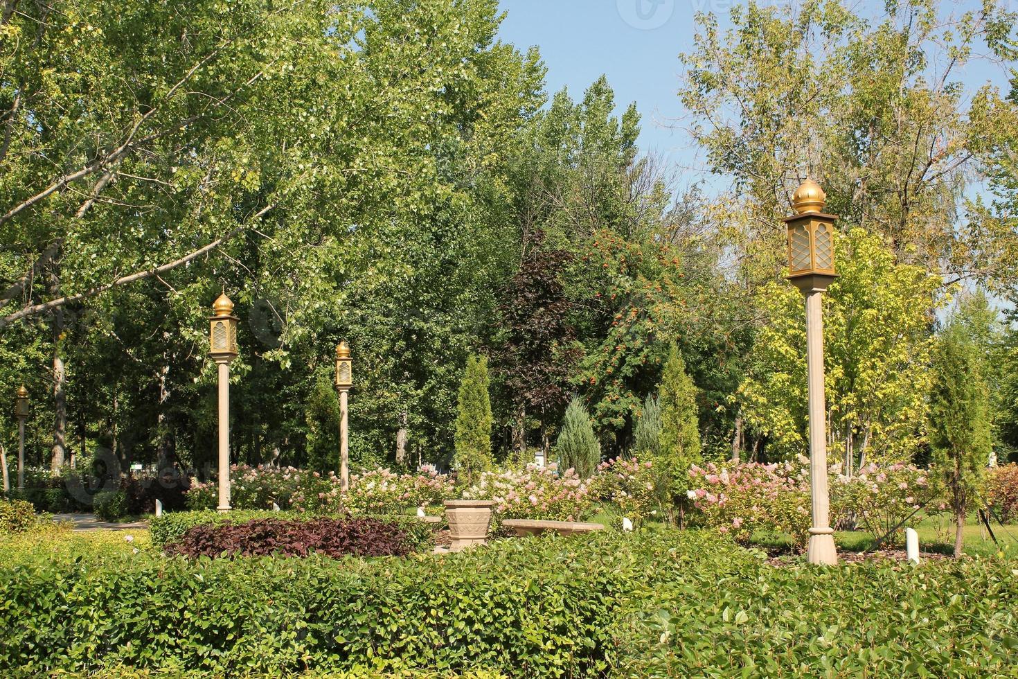 Trees and flowers in city park with Indian style lantern. Pedestrian zone for walking. Urban planning, public space concept. Town recreation area. Architecture design comfortable garden. Footpath way photo