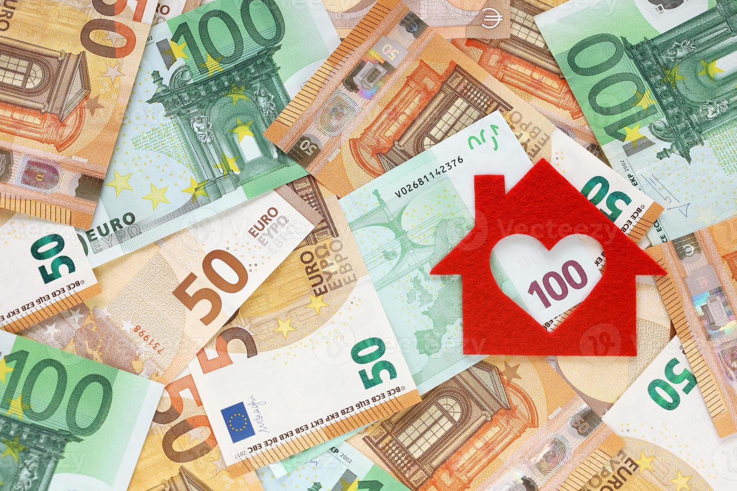 Red felt small house on right side of 50 and 100 euro banknotes background. Heart-shaped hole is cut instead of a window. Real estate loan concept. Money for a dream house. Top view. Place for text. photo