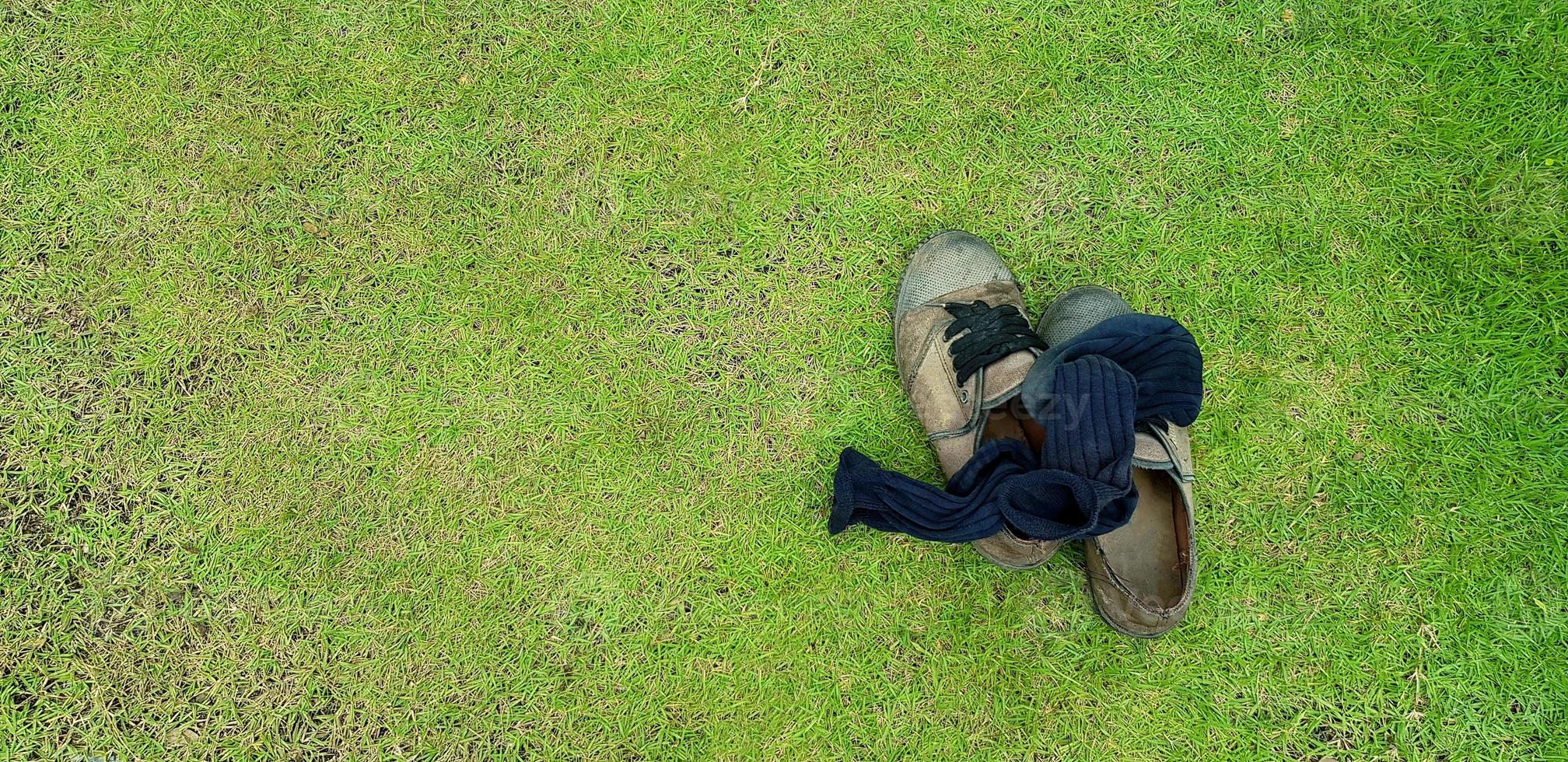 Top view of old shoes and black socks putting on green grass field background with left copy space. Used object and Life style concept photo