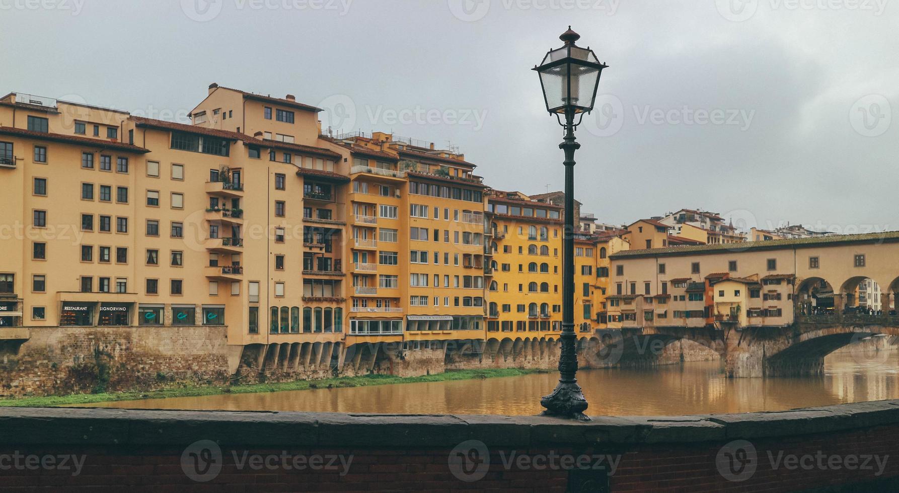 Detail of old town medieval bridge over gloomy waters and yellow buildings with light post in center photo