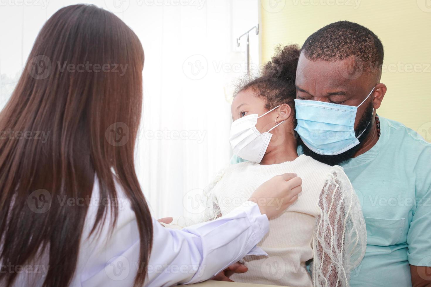 Asian female doctor uses a stethoscope Check the heartbeat of a little African-American girl sitting with her father. Concept of treatment for infectious diseases in children, during Coronavirus photo