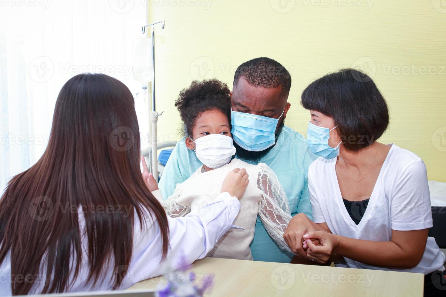 un mujer médico usado un estetoscopio a cheque el latido del corazón de un pequeño afroamericano niña sentado con su madre y padre. concepto de infeccioso enfermedad tratamiento en niños durante covid-19 foto