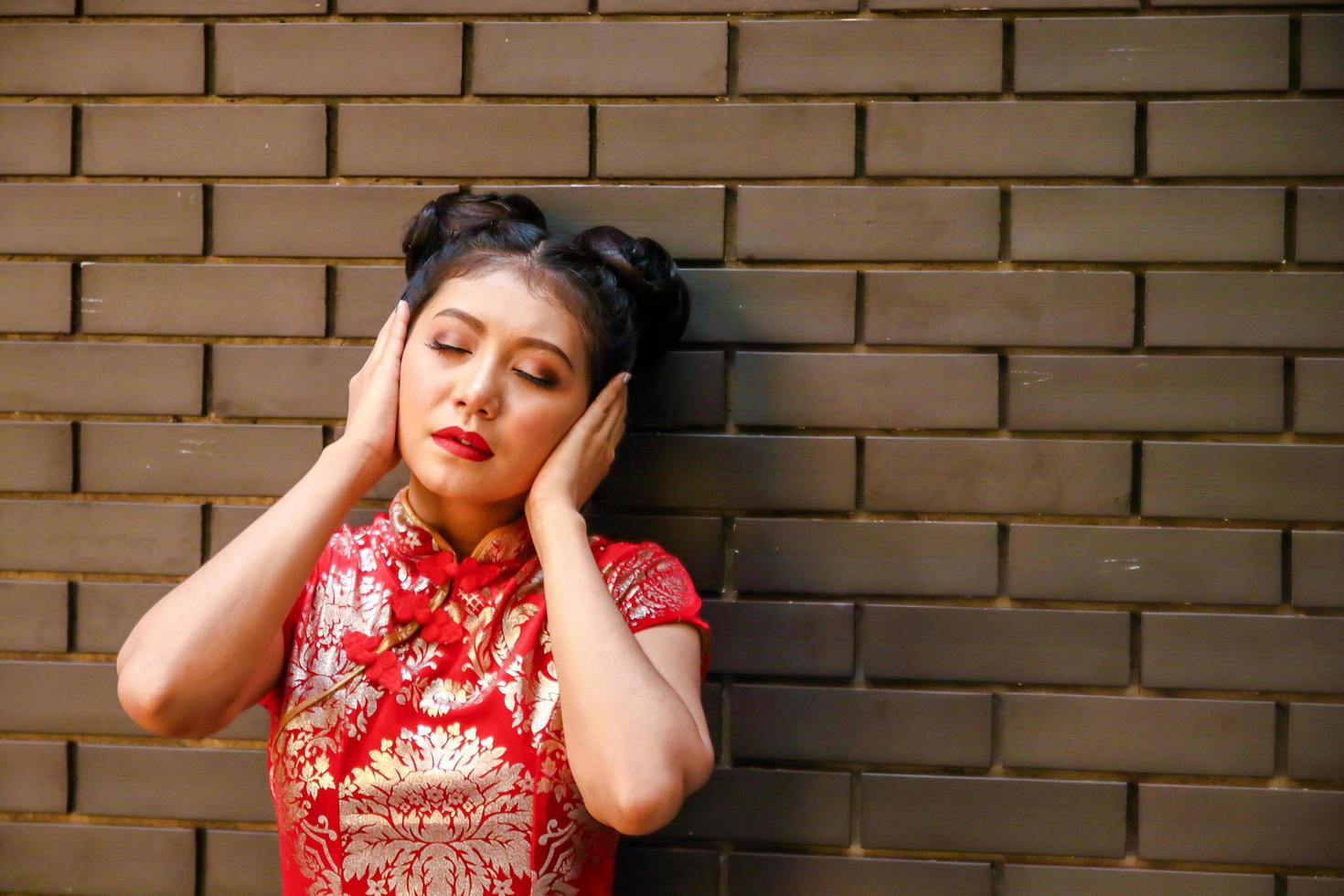 A Chinese woman wearing a red dress, covering her ears with both hands. New year festival photo