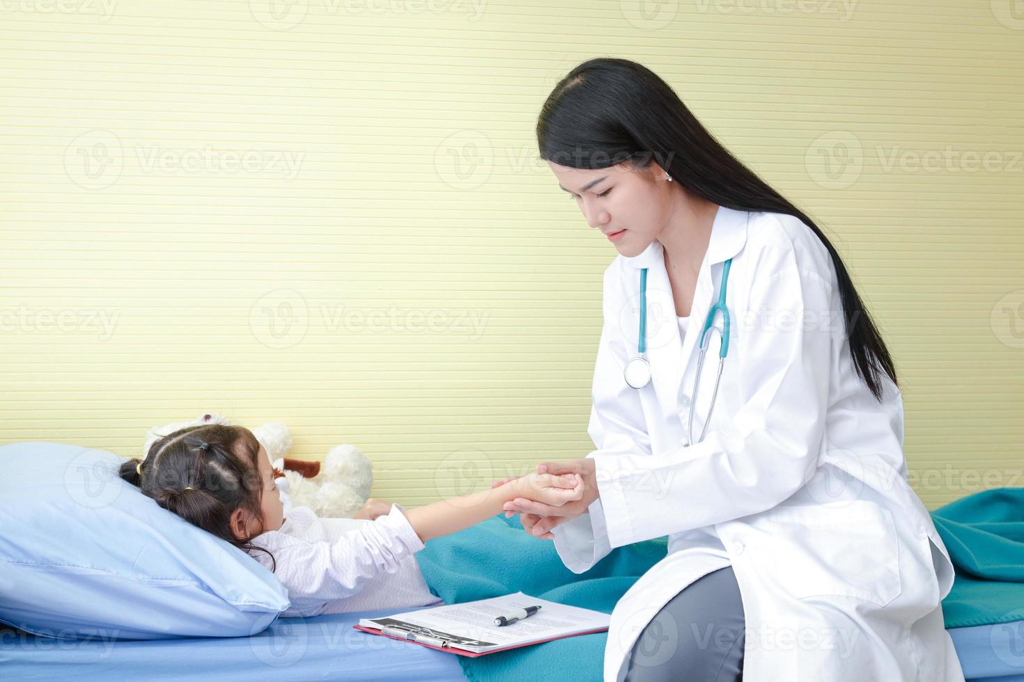 el médico usado un mano a sostener el legumbres en el Derecha muñeca de un pequeño niña en un hospital cama. niño cuidado conceptos foto