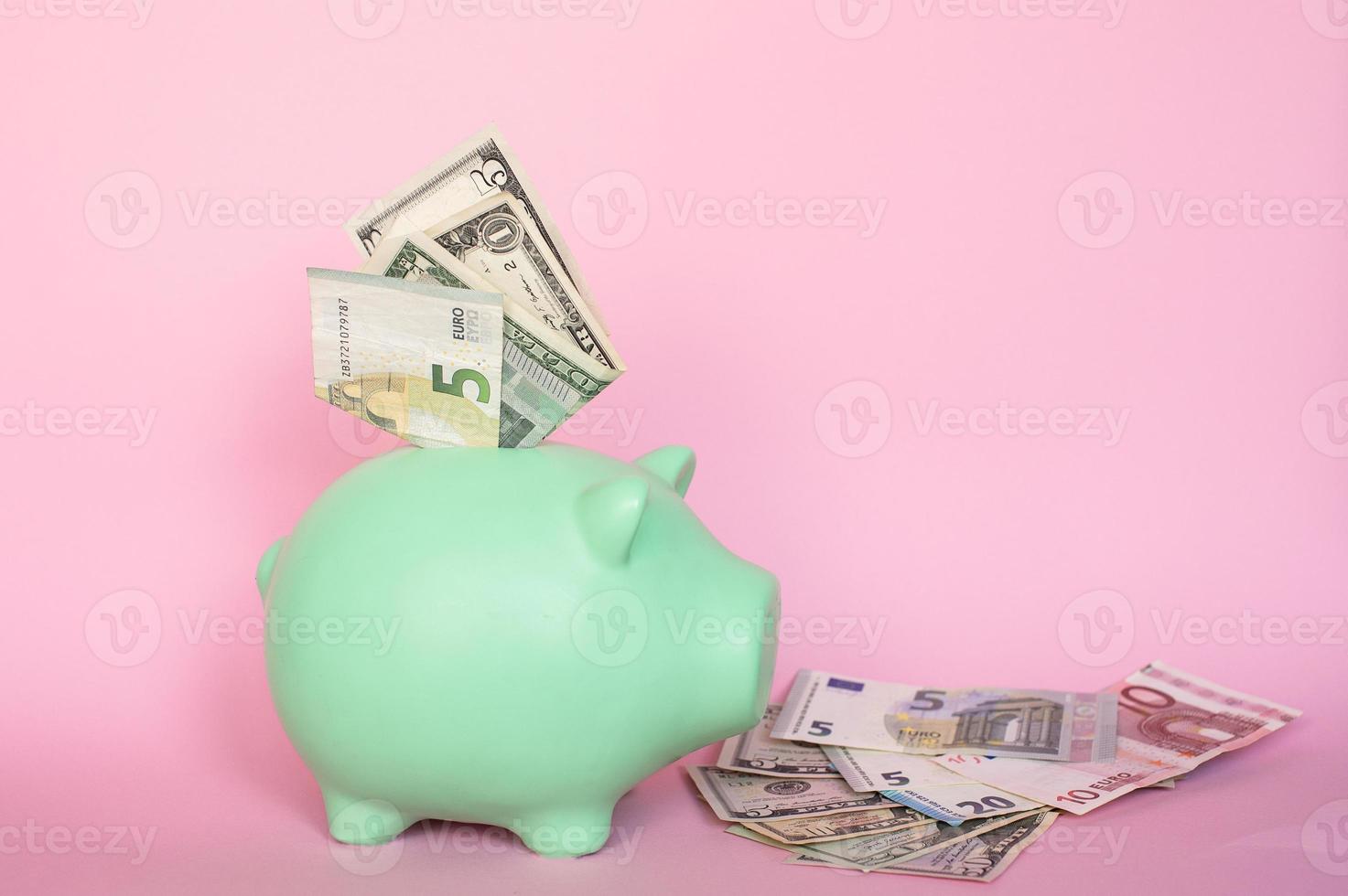 Banknotes of 5 and 10 euros and dollars on a pink background in a piggy bank photo